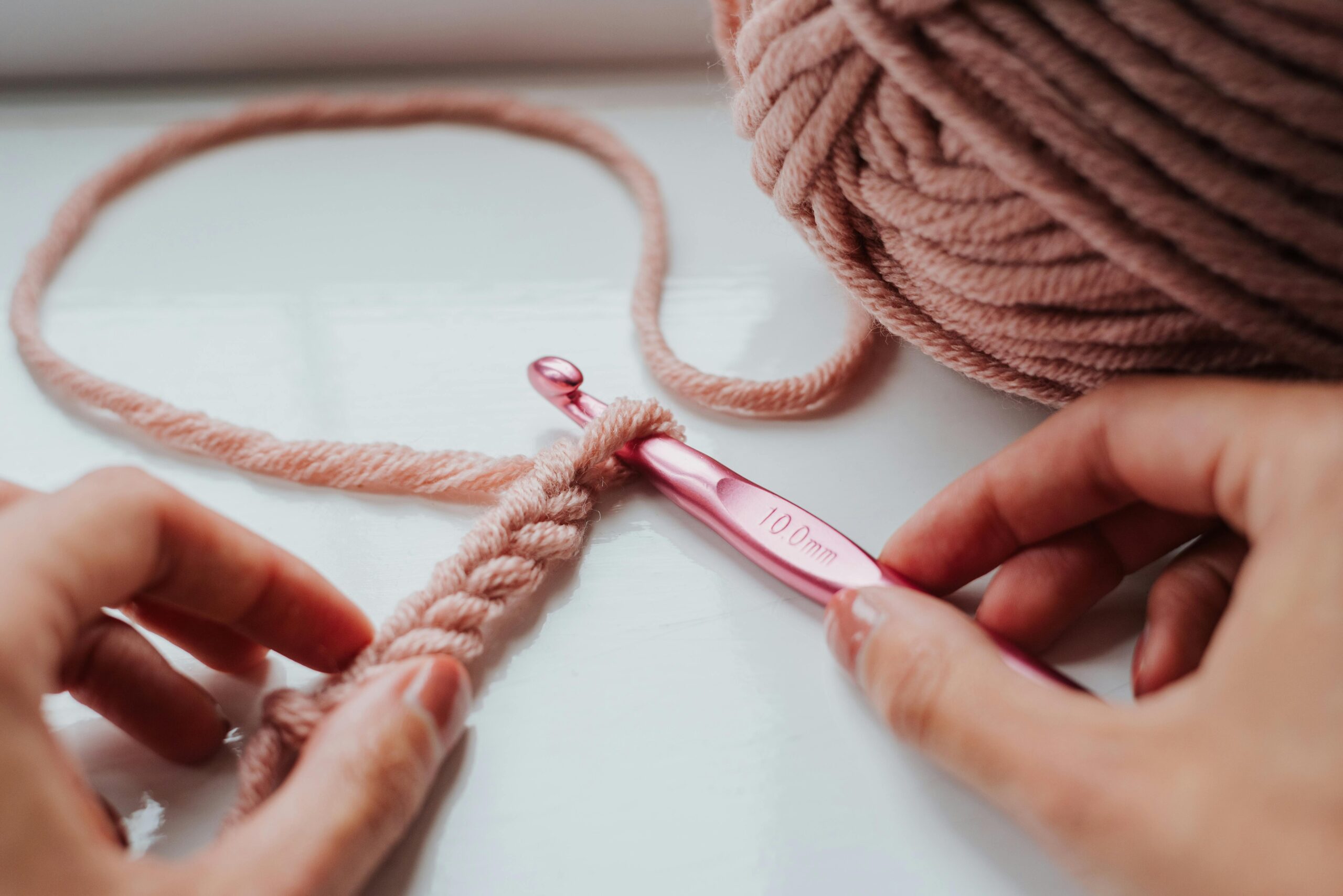 Mains crochetant avec du fil rose et un crochet de 10 mm sur un rebord de fenêtre confortable.